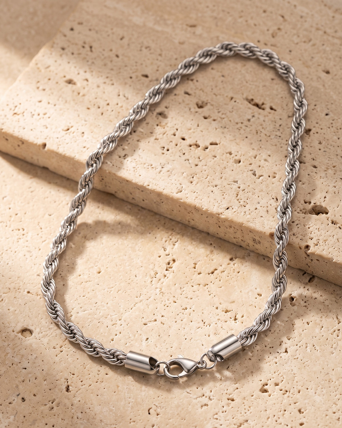 The whole silver Atlas fine rope chain lying on warm travertine stone