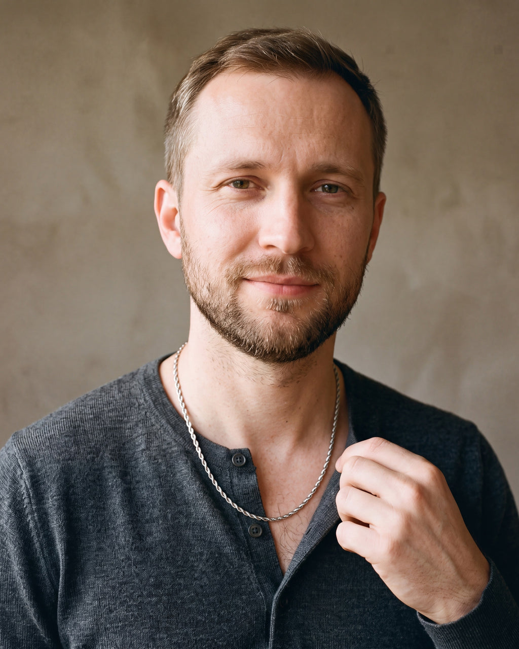 Man in a fine-gauge charcoal-grey merino knit with a henley neckline by a window wearing the silver Atlas fine rope chain