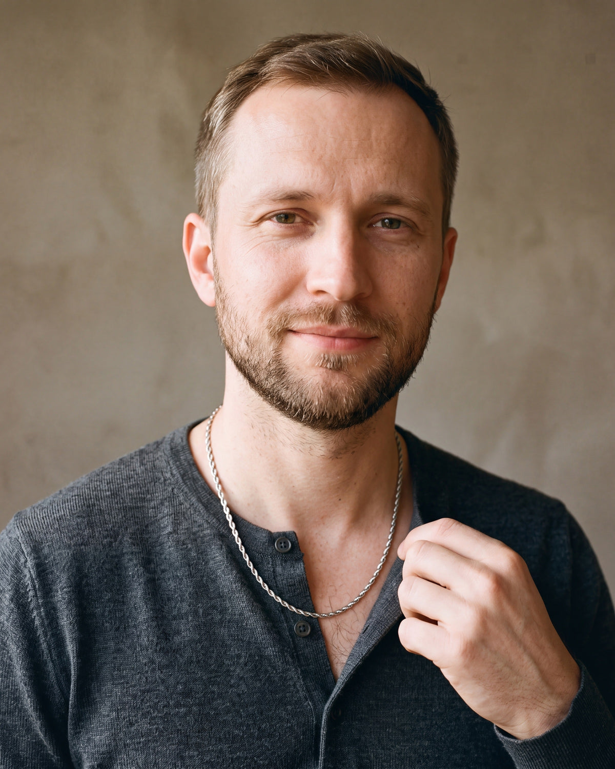 Man in a fine-gauge charcoal-grey merino knit with a henley neckline by a window wearing the silver Atlas fine rope chain