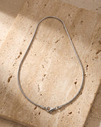 The whole silver-tone Atlas Fine Snake Chain lying on warm travertine stone