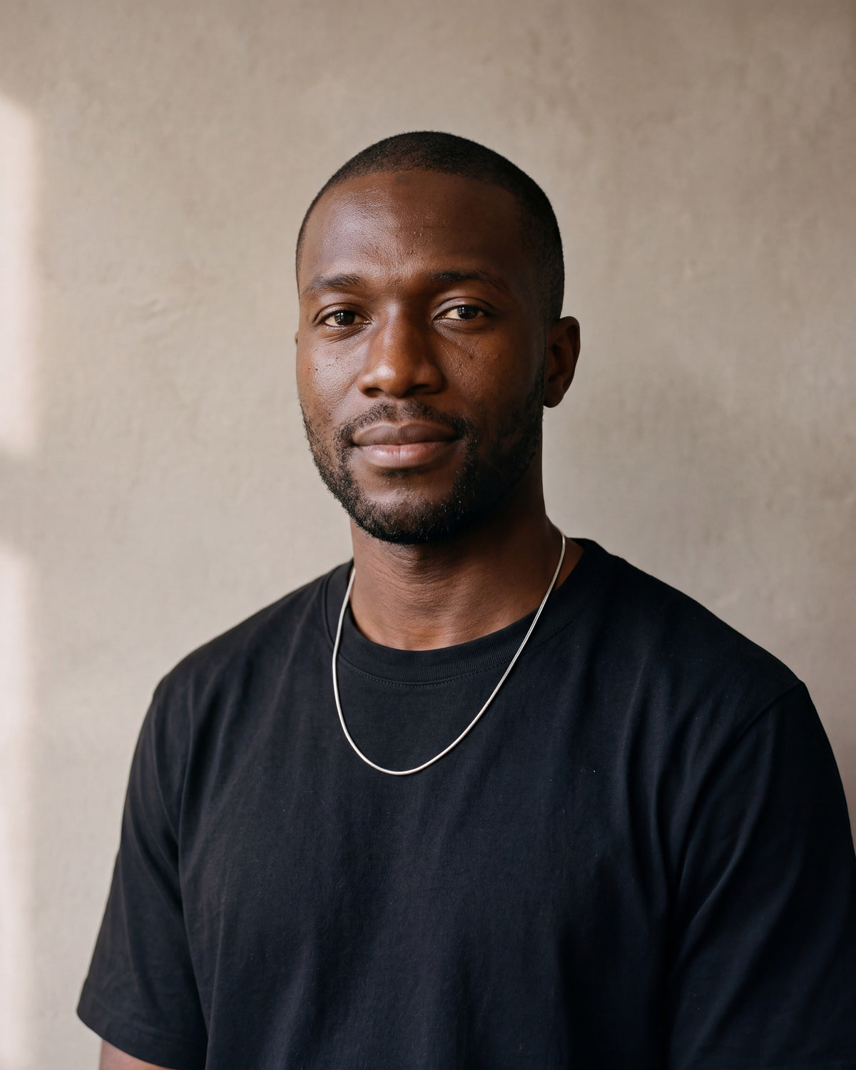 Man in a heavyweight black cotton crew-neck t-shirt by a window wearing the silver-tone Atlas Fine Snake Chain