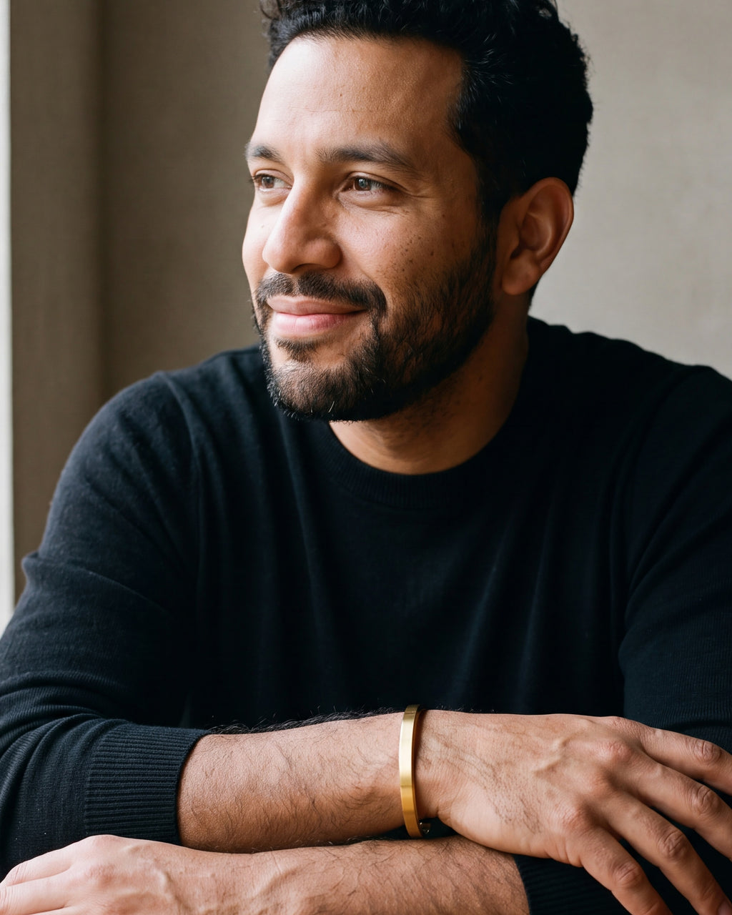 Man in a black sweater seated at a table, wearing the gold-tone Atlas flat cuff bracelet