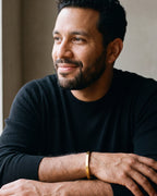 Man in a black sweater seated at a table, wearing the gold-tone Atlas flat cuff bracelet