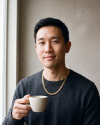 Man in a charcoal fine-gauge knit crew-neck sweater wearing the gold-tone Atlas Flat Curb Chain
