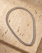 The whole silver Atlas Flat Curb Chain lying on warm travertine stone