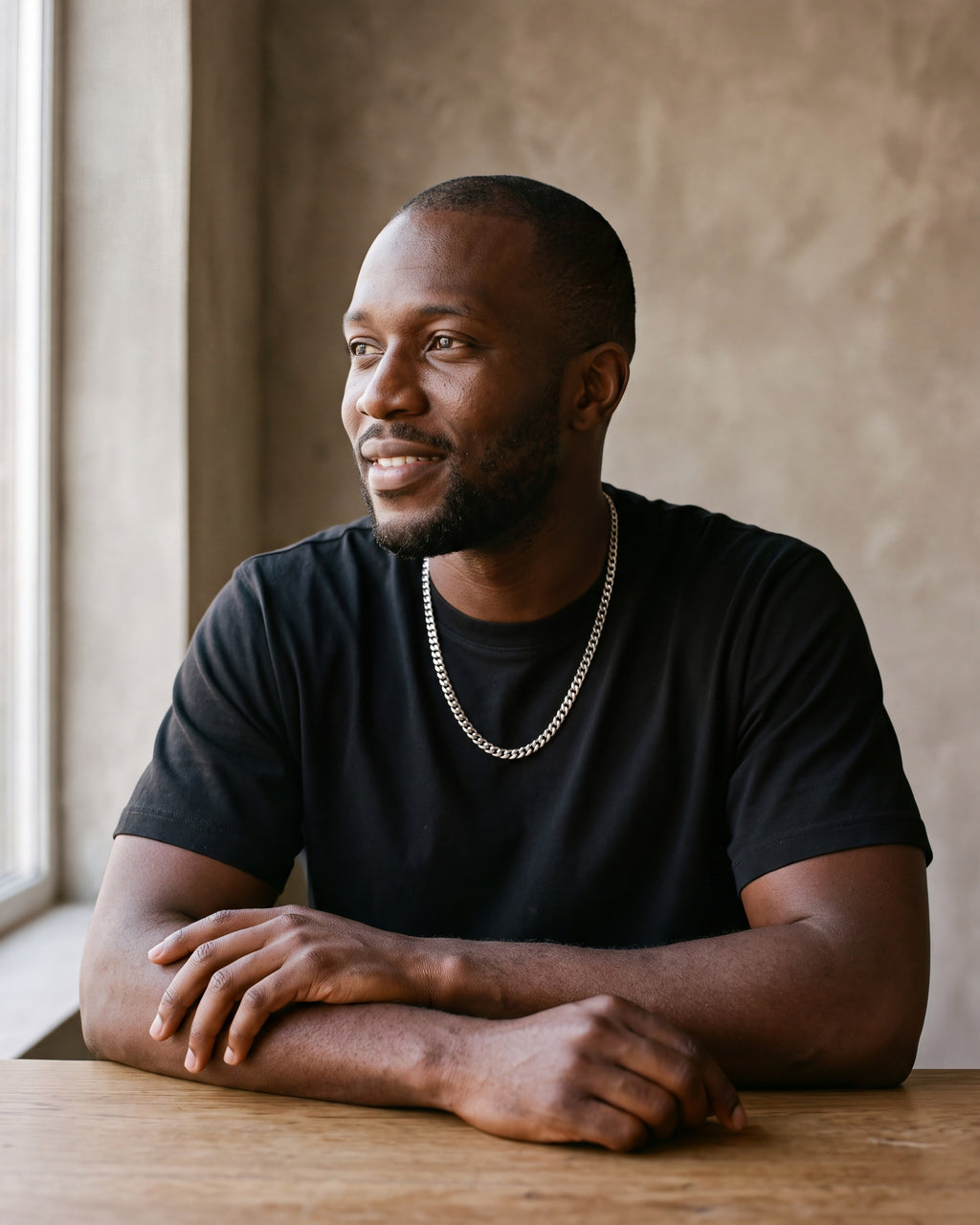 Man in a heavyweight black cotton crew-neck t-shirt by a window wearing the silver Atlas Flat Curb Chain