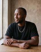 Man in a heavyweight black cotton crew-neck t-shirt by a window wearing the silver Atlas Flat Curb Chain