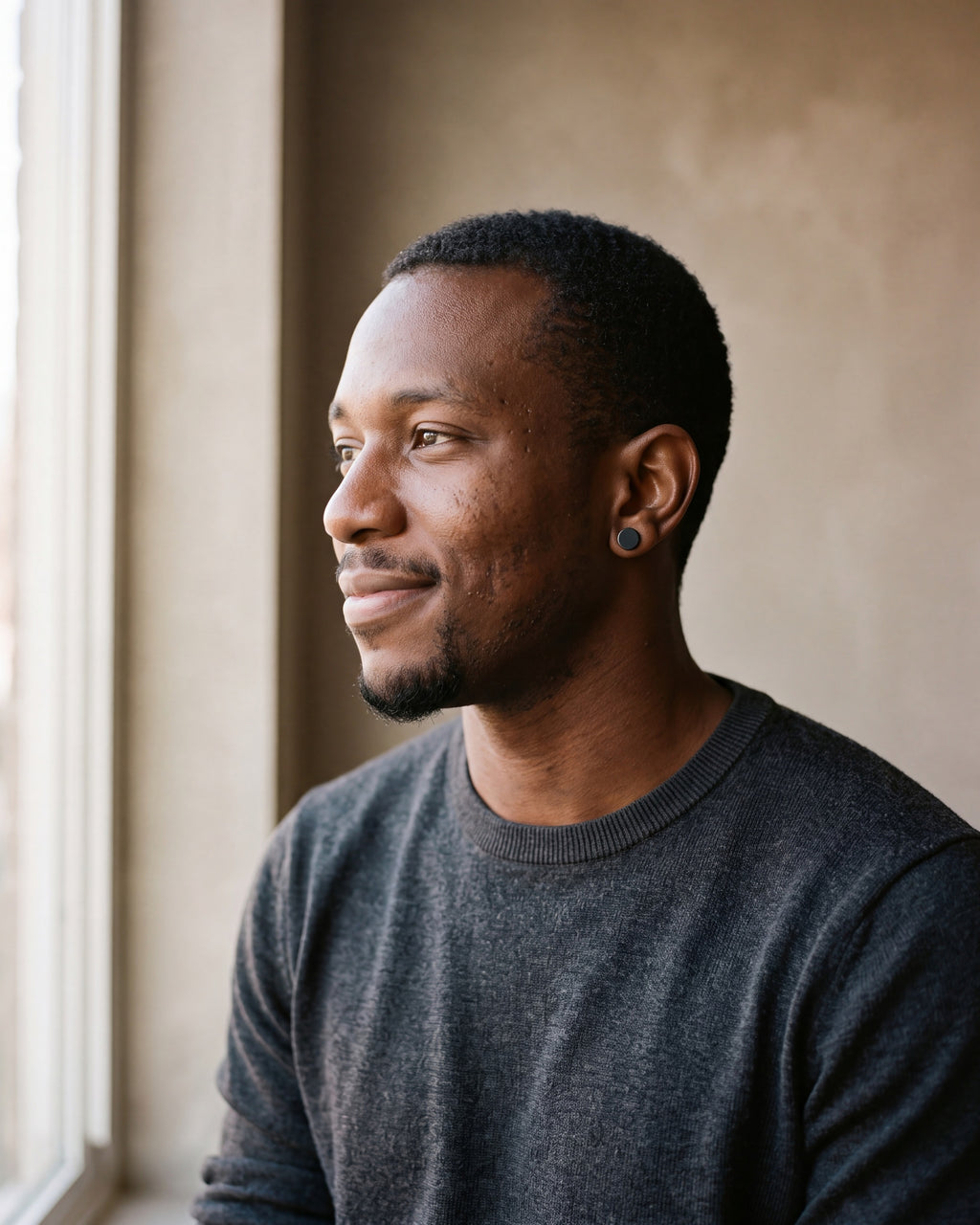 Man in a charcoal knit sweater wearing the Atlas flat disc barbell stud earrings in black steel