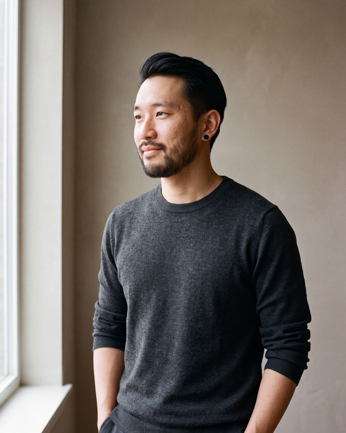 Man in a charcoal sweater with his hands in his pockets wearing the black Atlas flat disc stud earrings