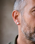 Close-up of the silver-tone Atlas flat disc stud earrings worn by a man, shown at true size
