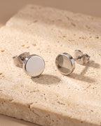 The whole silver-tone Atlas flat disc stud earrings laid on warm stone
