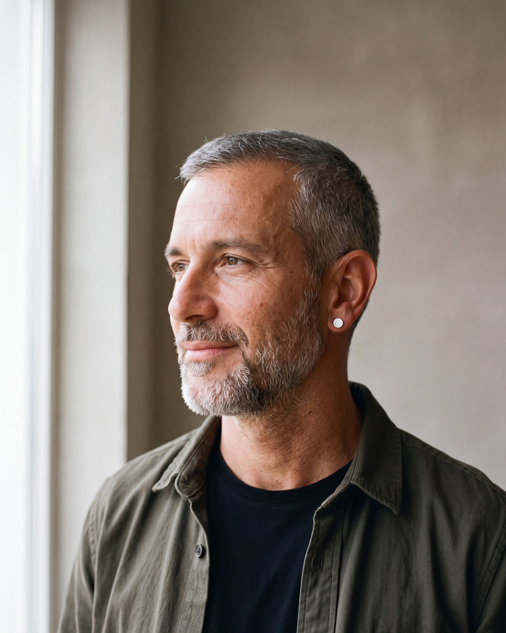 Man in an olive overshirt seen in profile wearing the silver-tone Atlas flat disc stud earrings