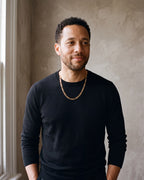 Man in a black merino crew-neck sweater by a window wearing the gold-tone Atlas Flat Gold-Tone Figaro Chain