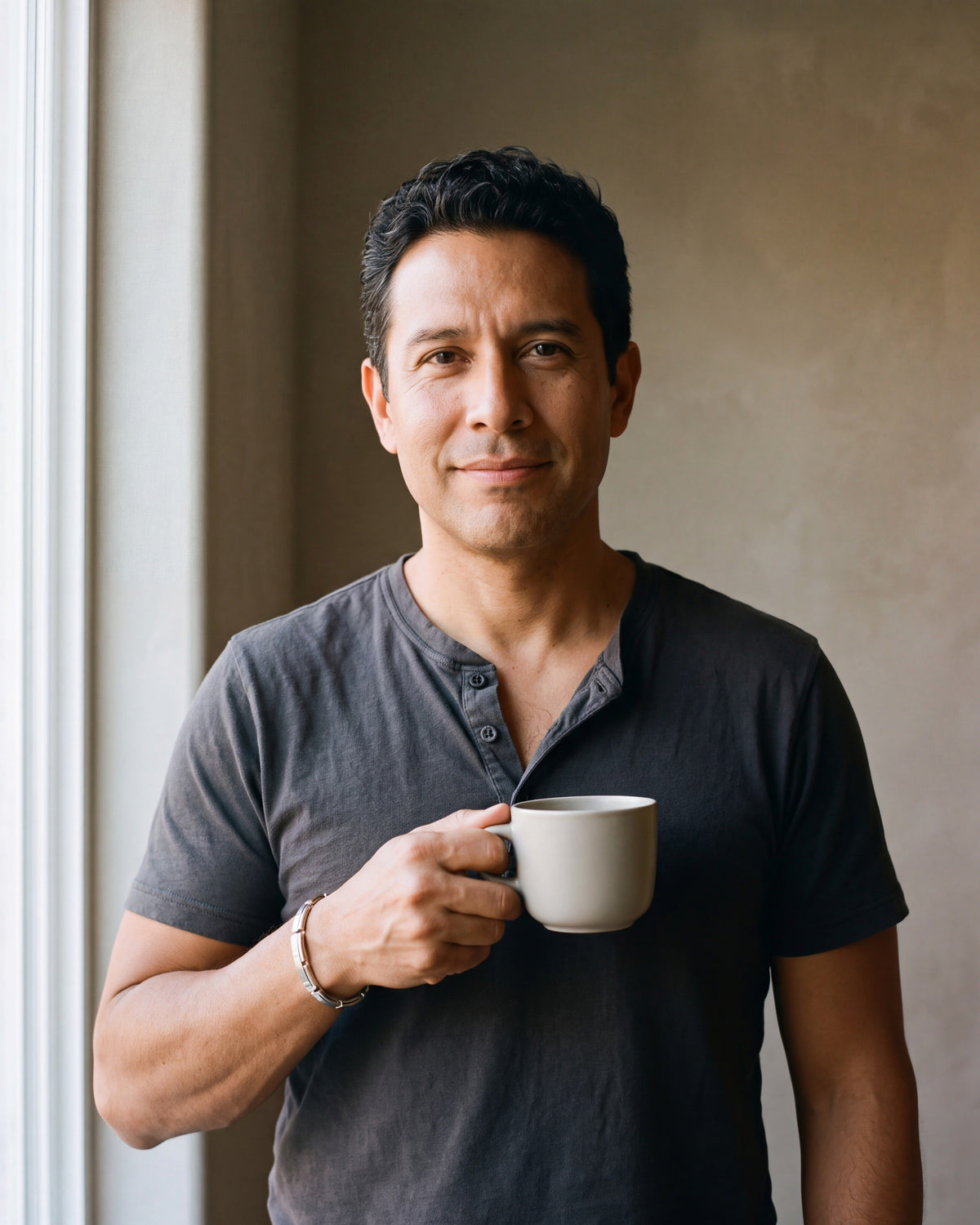 Man in a charcoal henley holding a coffee cup wearing the silver-tone Atlas geometric cuff bracelet