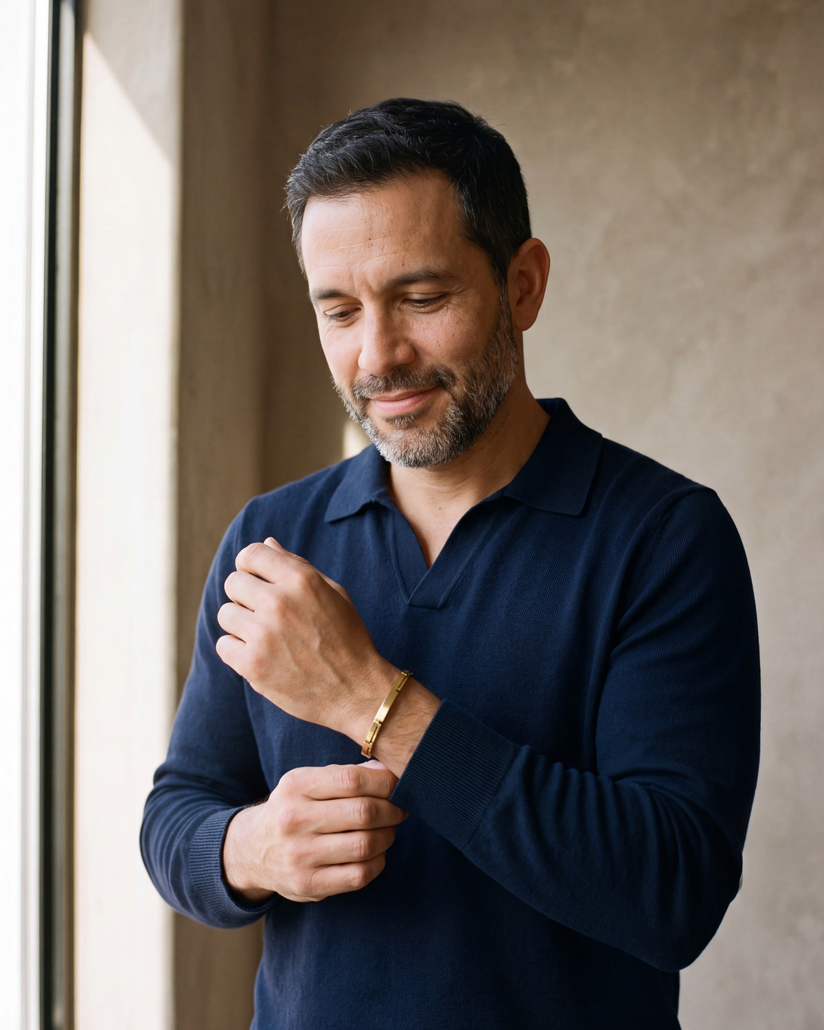 Man in a navy shirt adjusting his cuff, wearing the gold-tone Atlas geometric link cuff