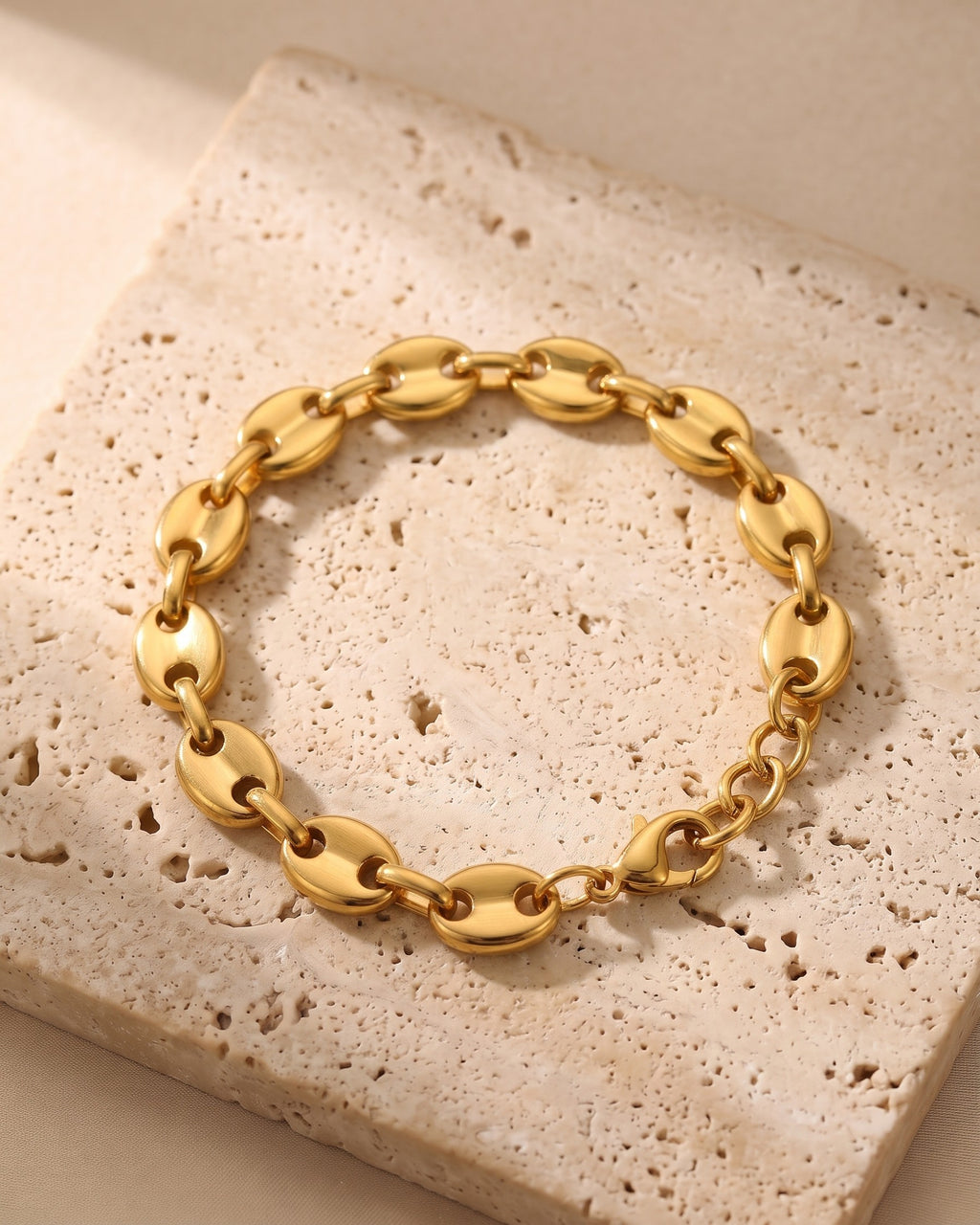 The gold-tone Atlas Gold-Tone Coffee Bean Link Bracelet laid on warm travertine stone