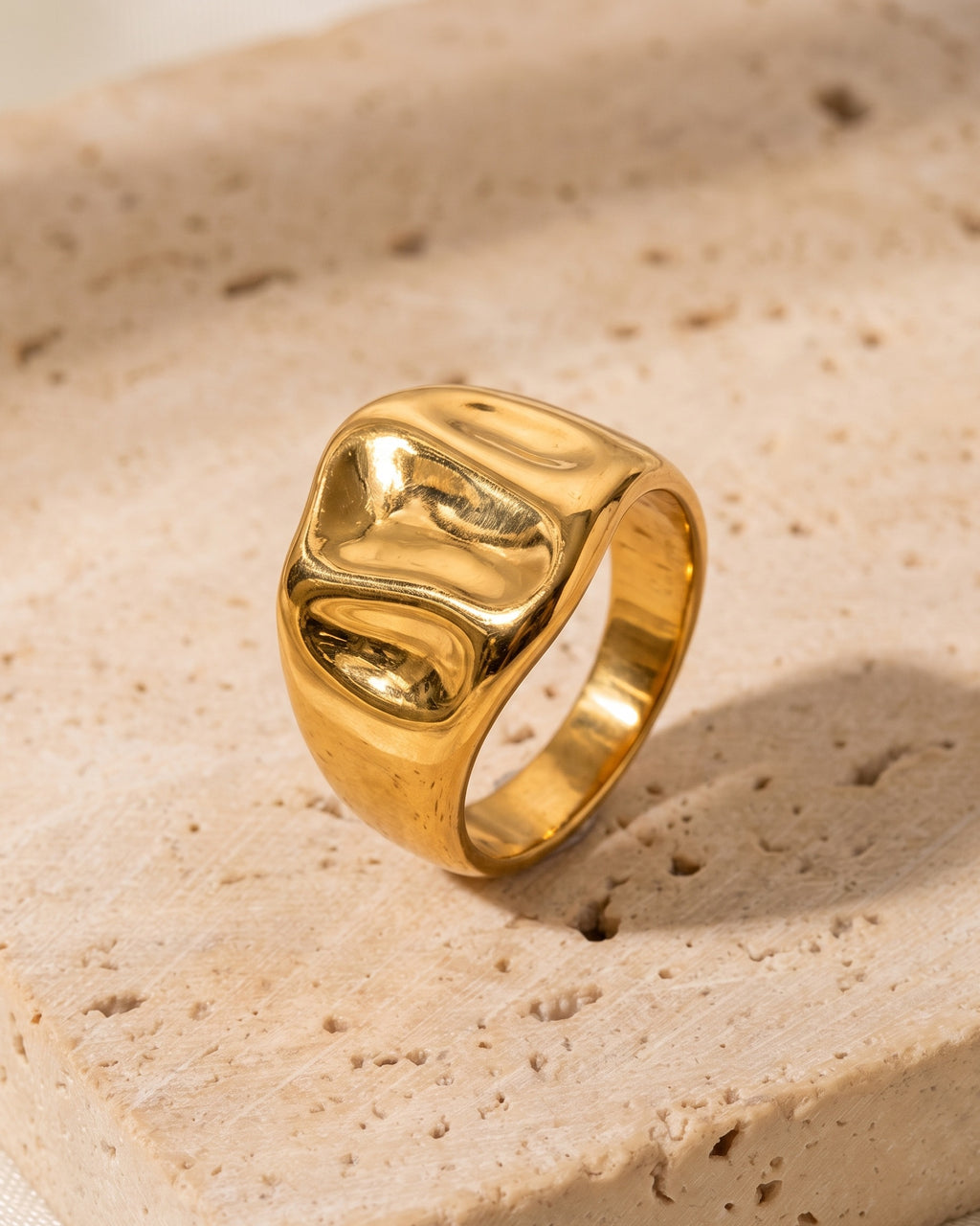 The Atlas gold-tone hammered wide face signet ring standing on warm stone