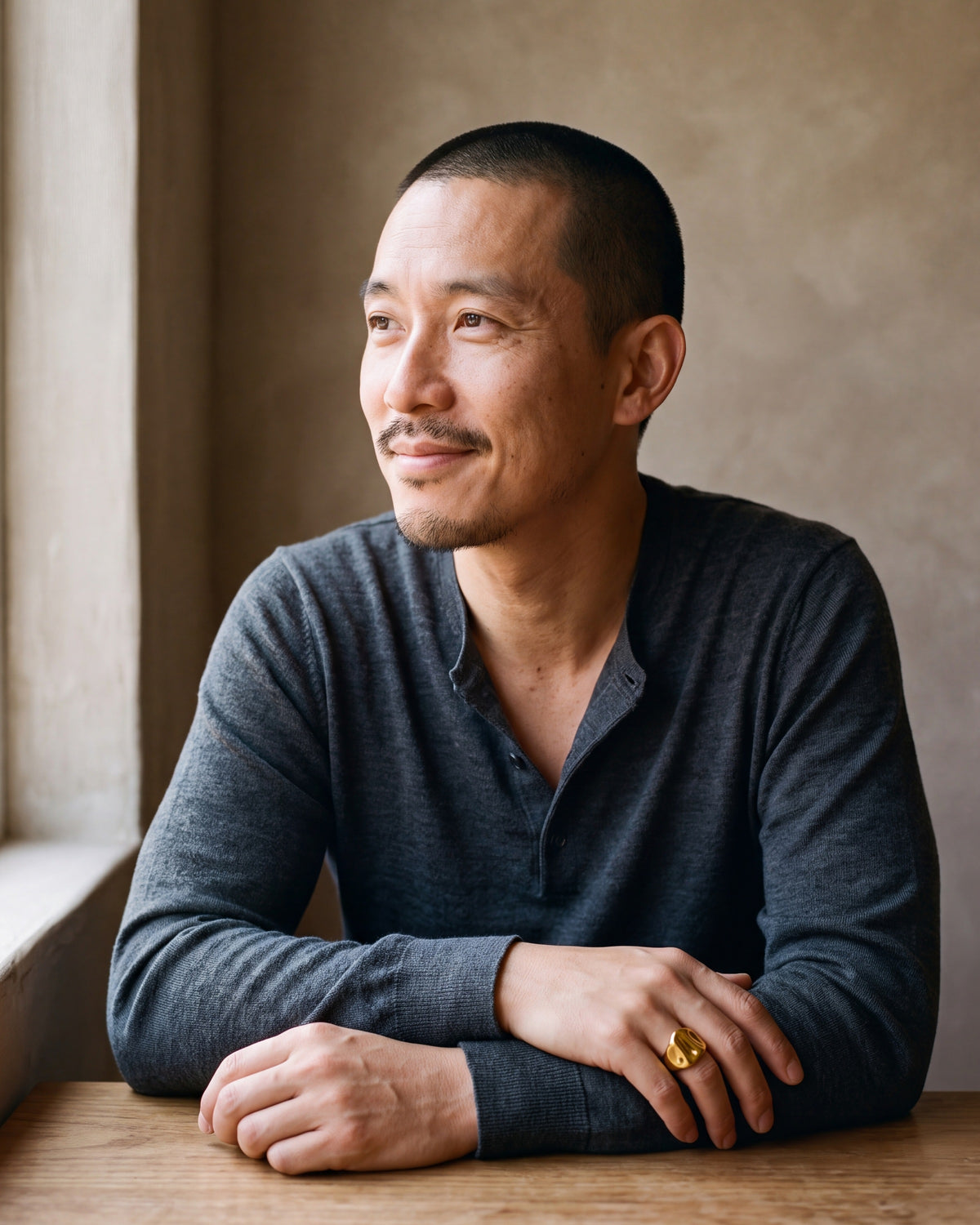 Man in a charcoal henley seated at a table, wearing the Atlas gold-tone hammered signet ring on his little finger