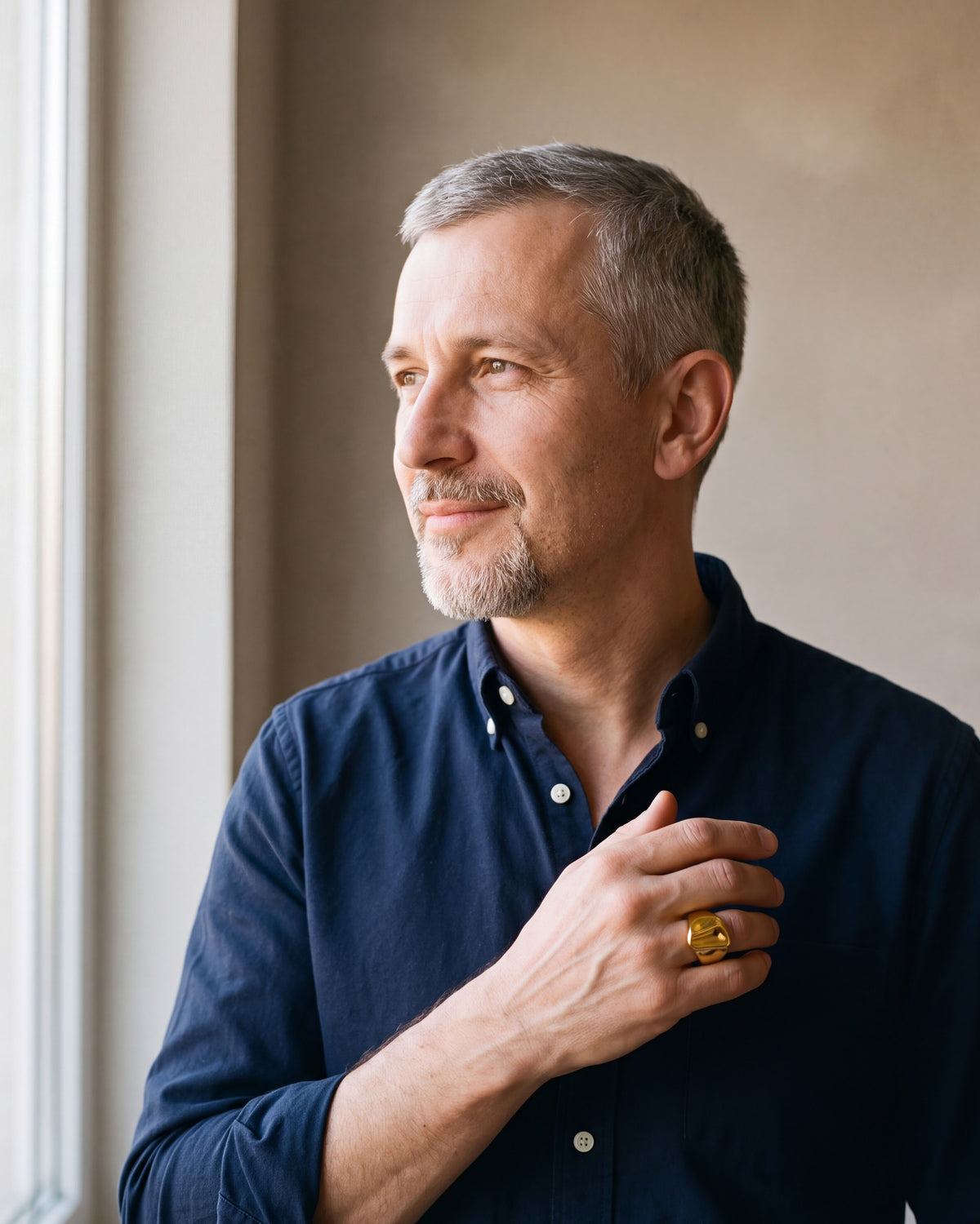 Man in a navy shirt by a window wearing the Atlas gold-tone hammered signet ring