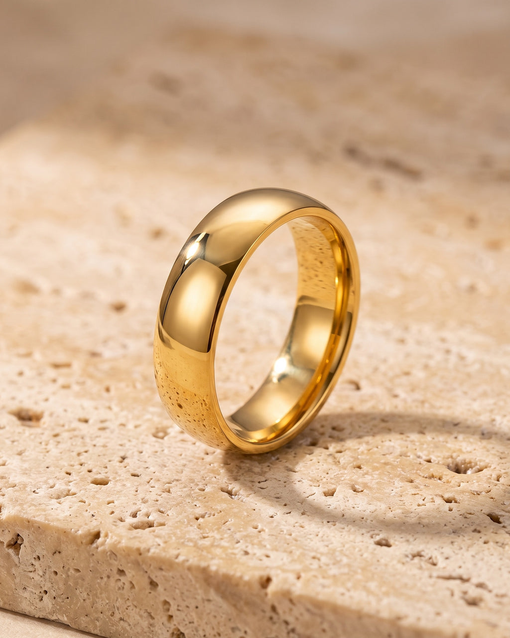 Entire Atlas polished dome band in gold-tone steel, lying flat on warm stone
