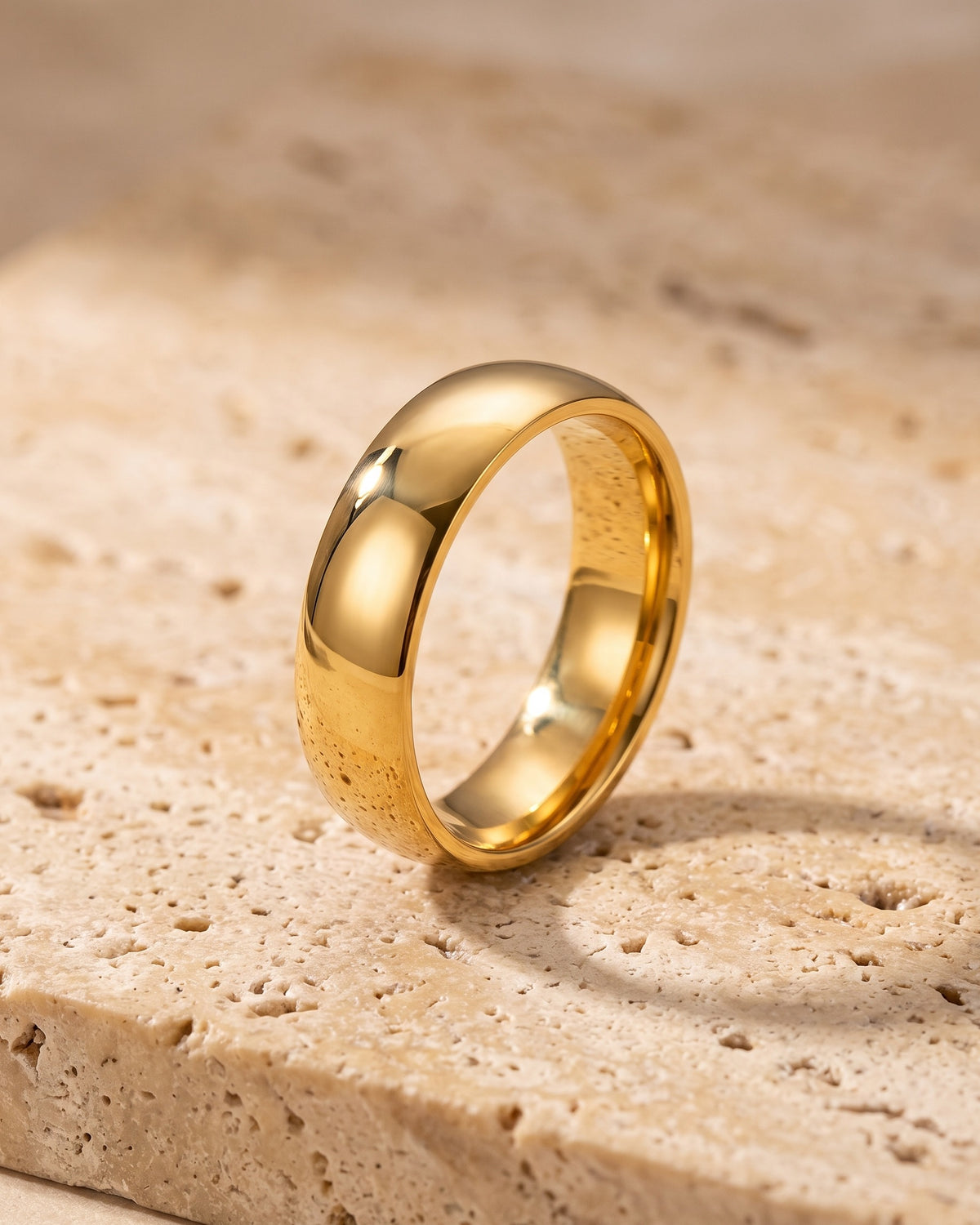 Entire Atlas polished dome band in gold-tone steel, lying flat on warm stone