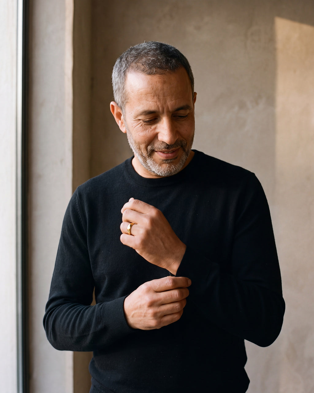 Man in a black merino sweater by a window wearing the Atlas polished dome band in gold-tone steel