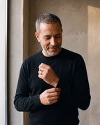 Man in a black merino sweater by a window wearing the Atlas polished dome band in gold-tone steel
