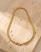The whole gold-tone Atlas gold-tone rope chain lying on warm travertine stone