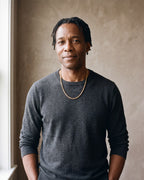 Man in a charcoal fine-gauge knit crew-neck sweater by a window wearing the gold-tone Atlas gold-tone rope chain