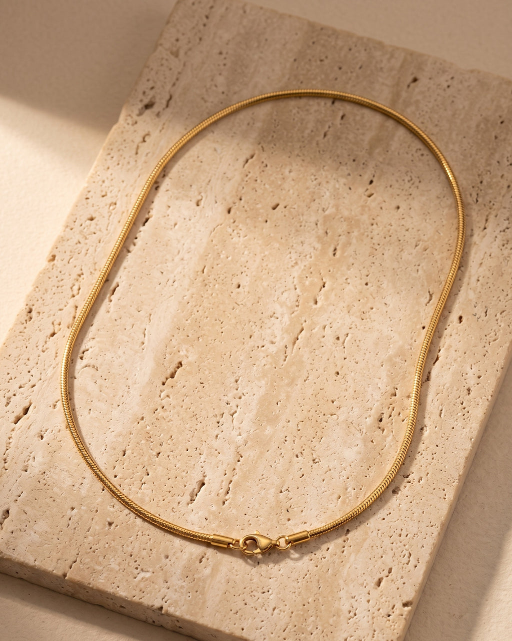 The whole Atlas gold-tone snake chain on warm stone, lobster clasp