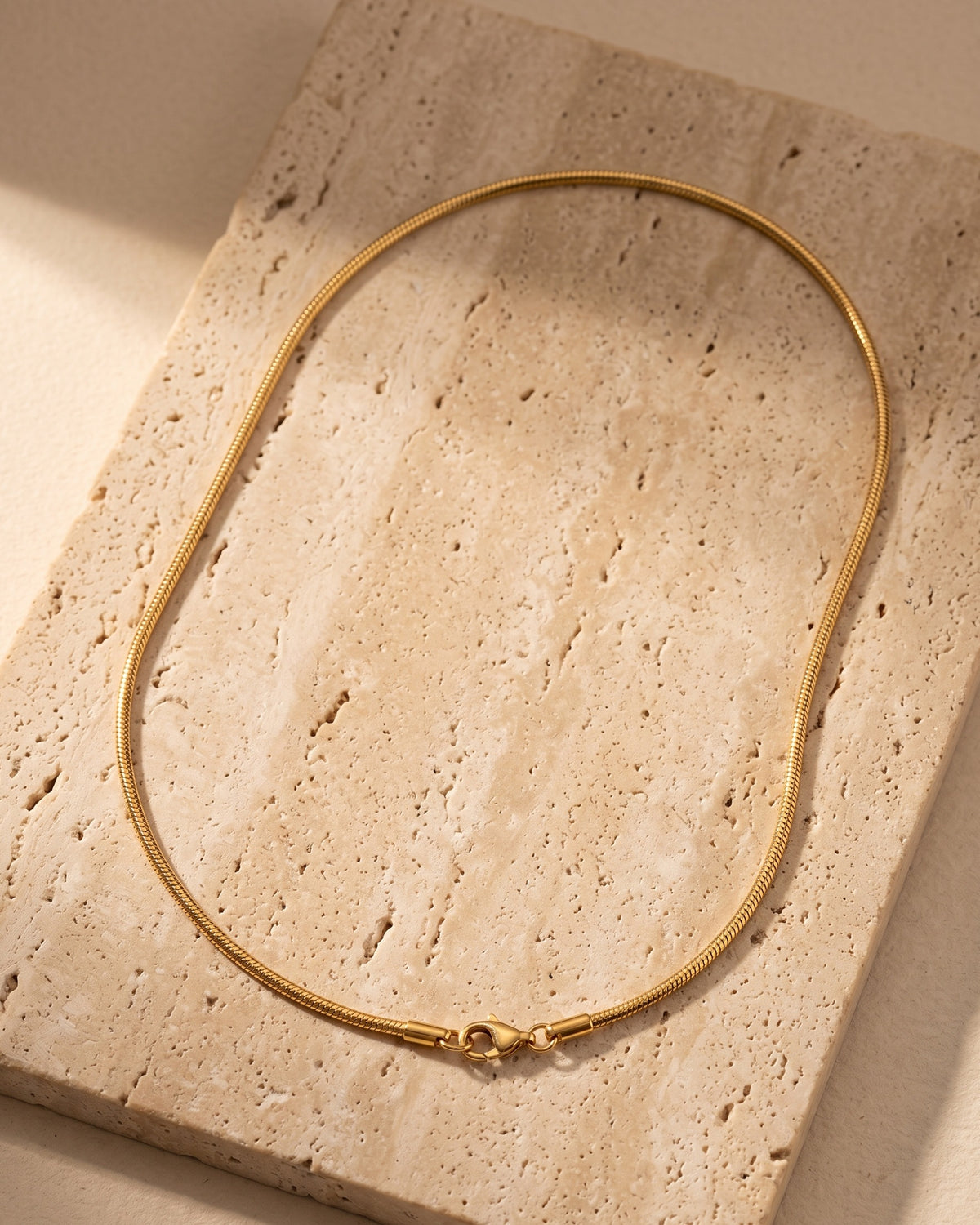The whole Atlas gold-tone snake chain on warm stone, lobster clasp