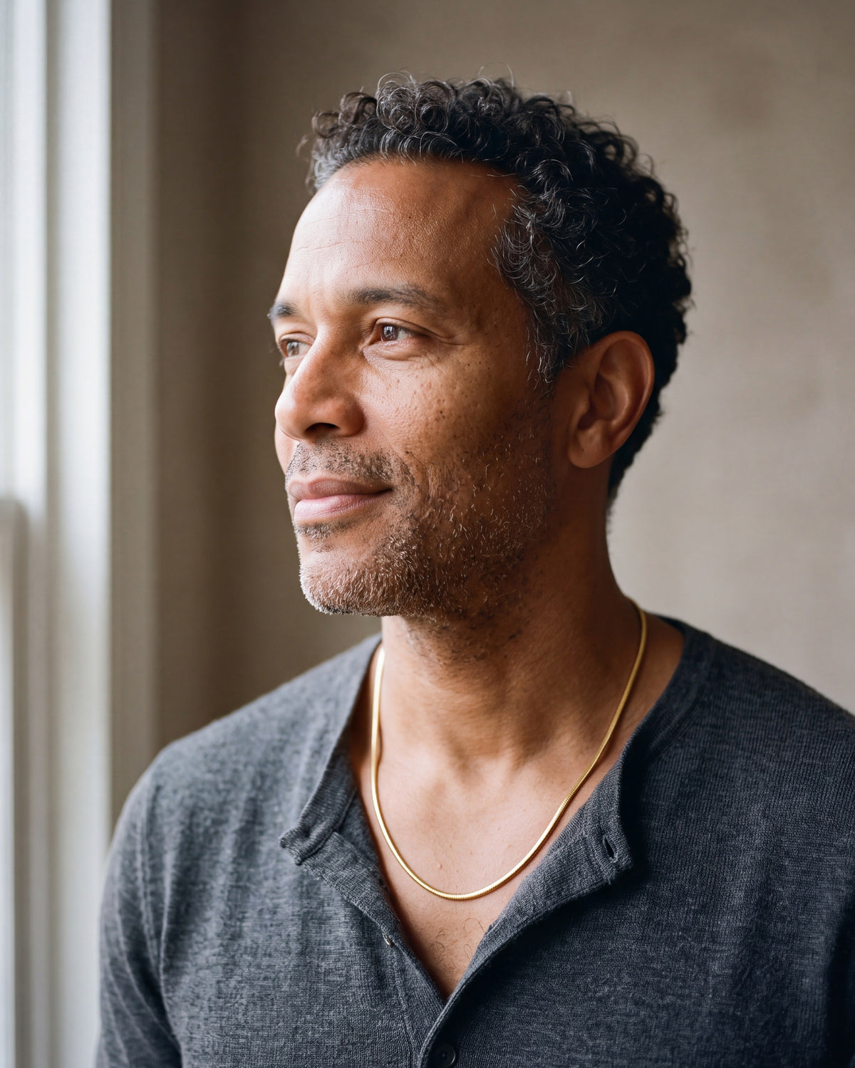 Man in a charcoal henley by a window wearing the Atlas gold-tone snake chain