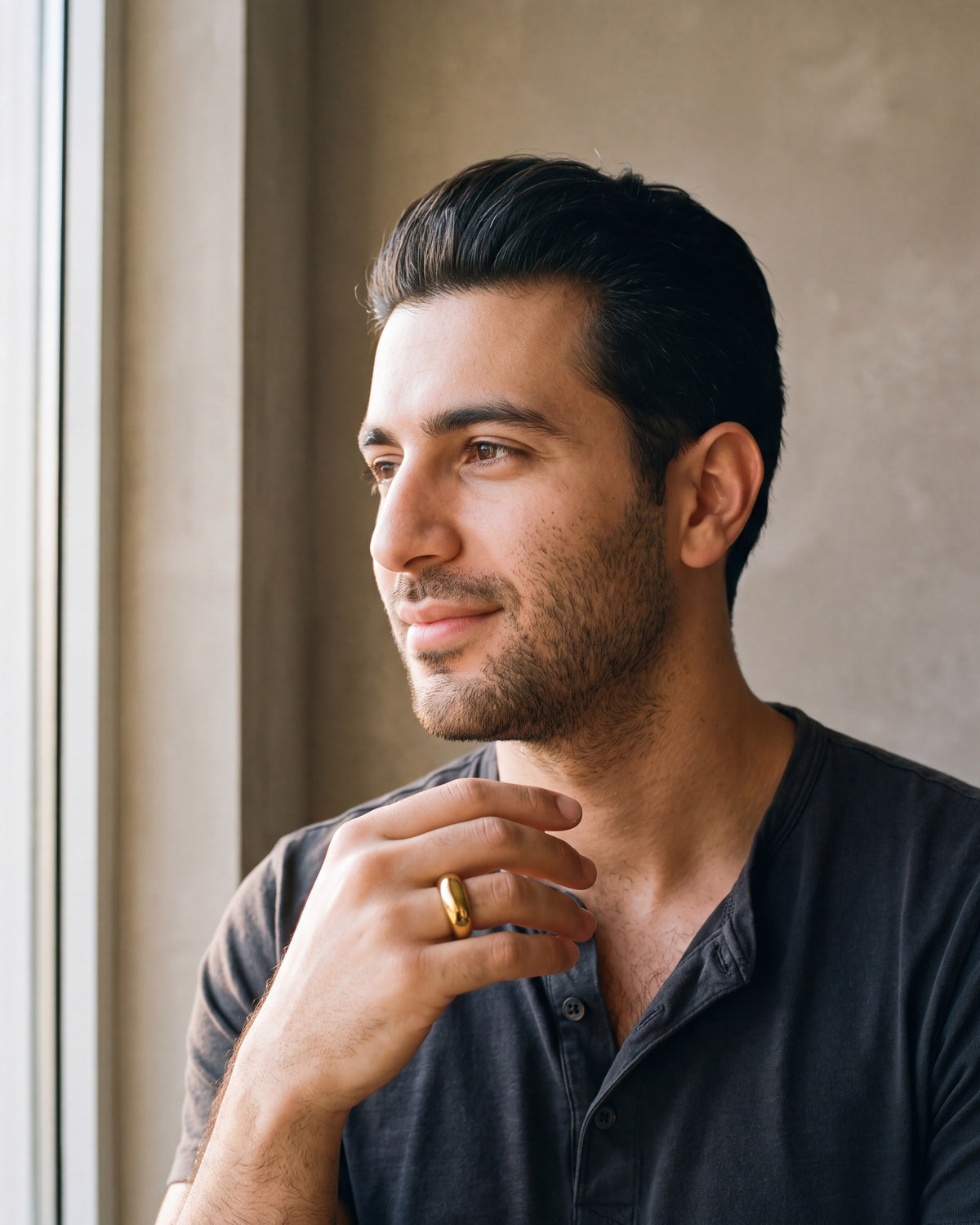 Man in a charcoal cotton henley t-shirt by a window wearing the gold-tone Atlas Gold-Tone Tapered Dome Ring