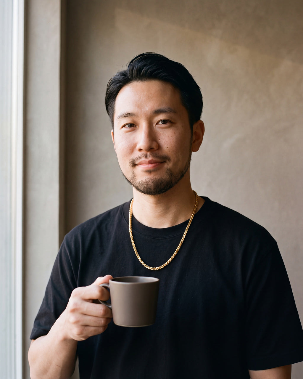 Man in a black T-shirt holding a coffee cup wearing the gold-tone Atlas gold-tone wheat chain