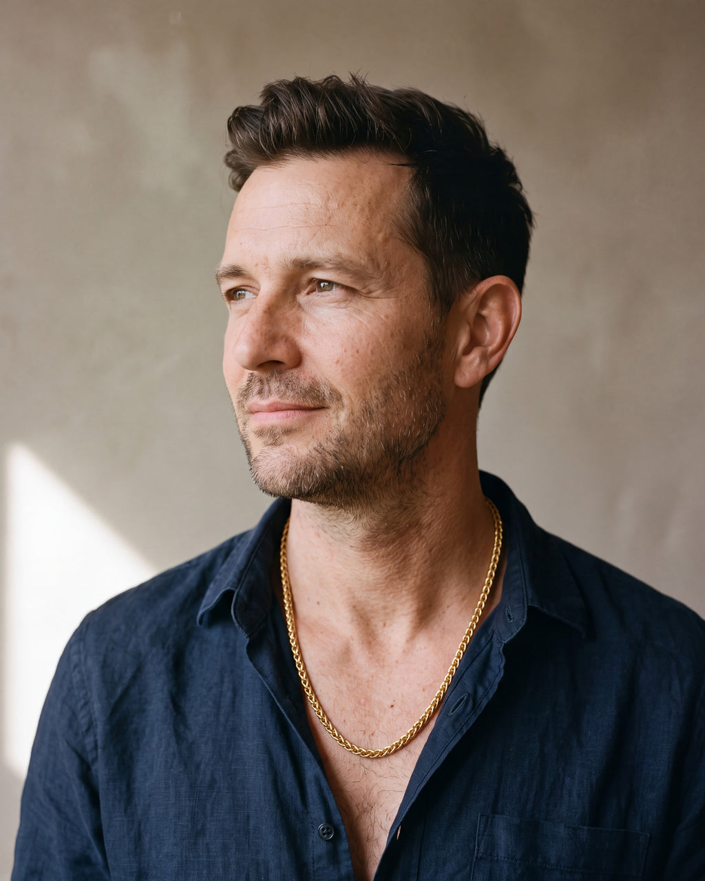 Man in a navy linen shirt seen in profile wearing the gold-tone Atlas gold-tone wheat chain