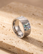 Silver Atlas hammered abalone inlay ring standing on warm stone