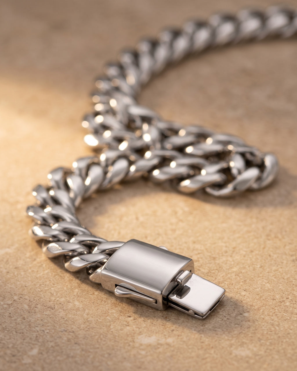 Close-up of the silver Atlas heavy Cuban chain and its push-button box clasp on warm stone