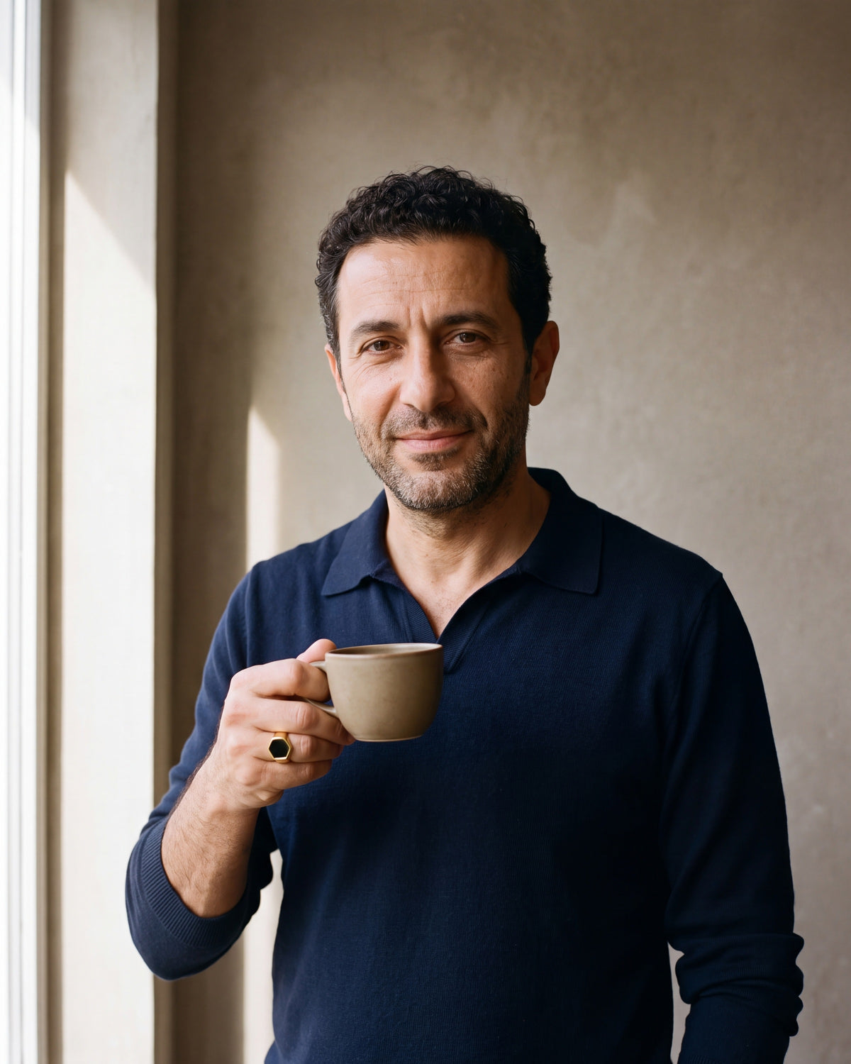 Man in a navy knit polo holding a coffee cup wearing the gold-tone Atlas hexagon signet ring