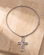 Silver-tone Atlas cut-out cross pendant and box chain laid whole on warm stone