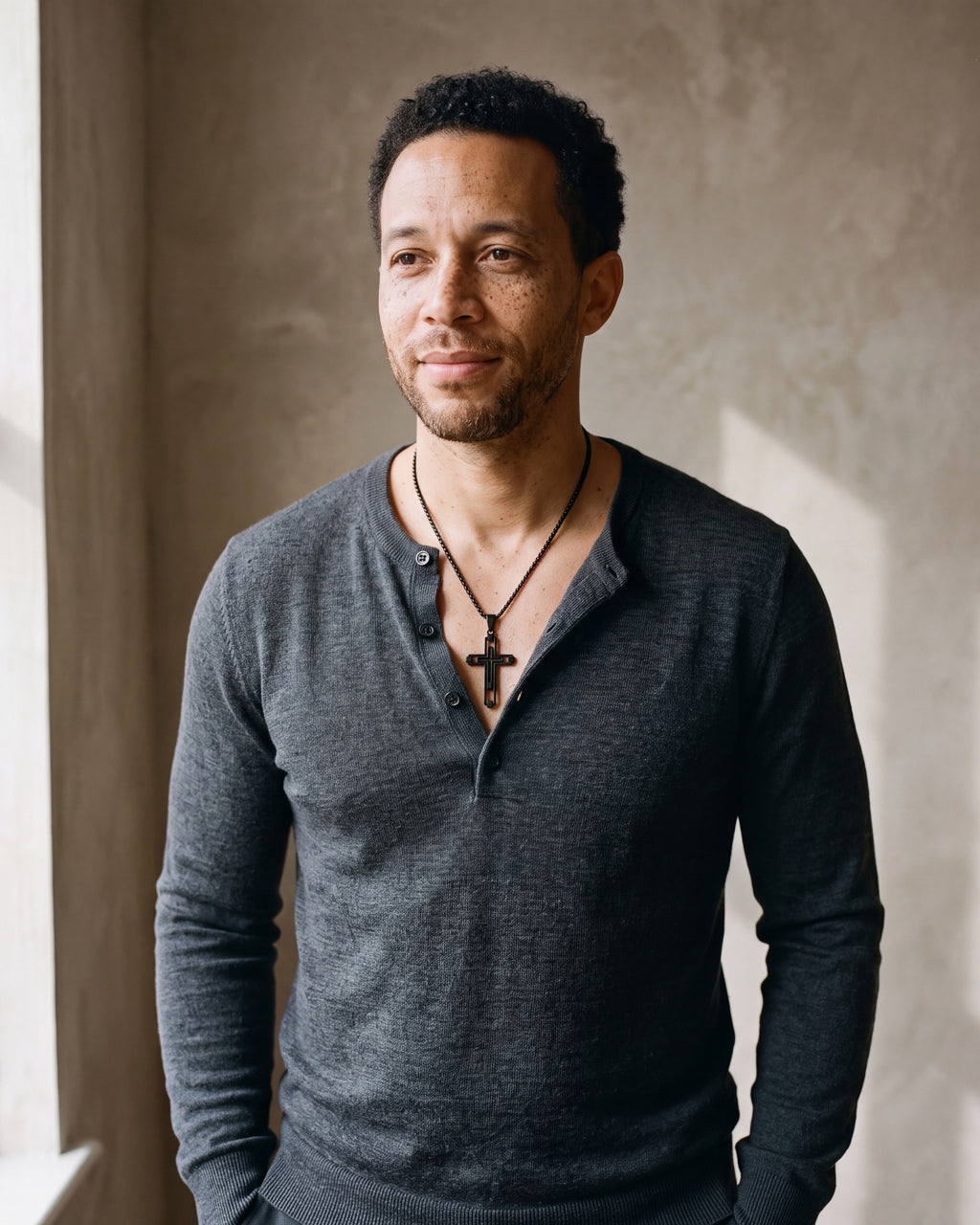 Man in a fine-gauge charcoal-grey merino knit with a henley neckline wearing the black Atlas Hollow Geometric Cross Necklace