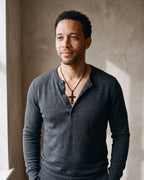 Man in a fine-gauge charcoal-grey merino knit with a henley neckline wearing the black Atlas Hollow Geometric Cross Necklace