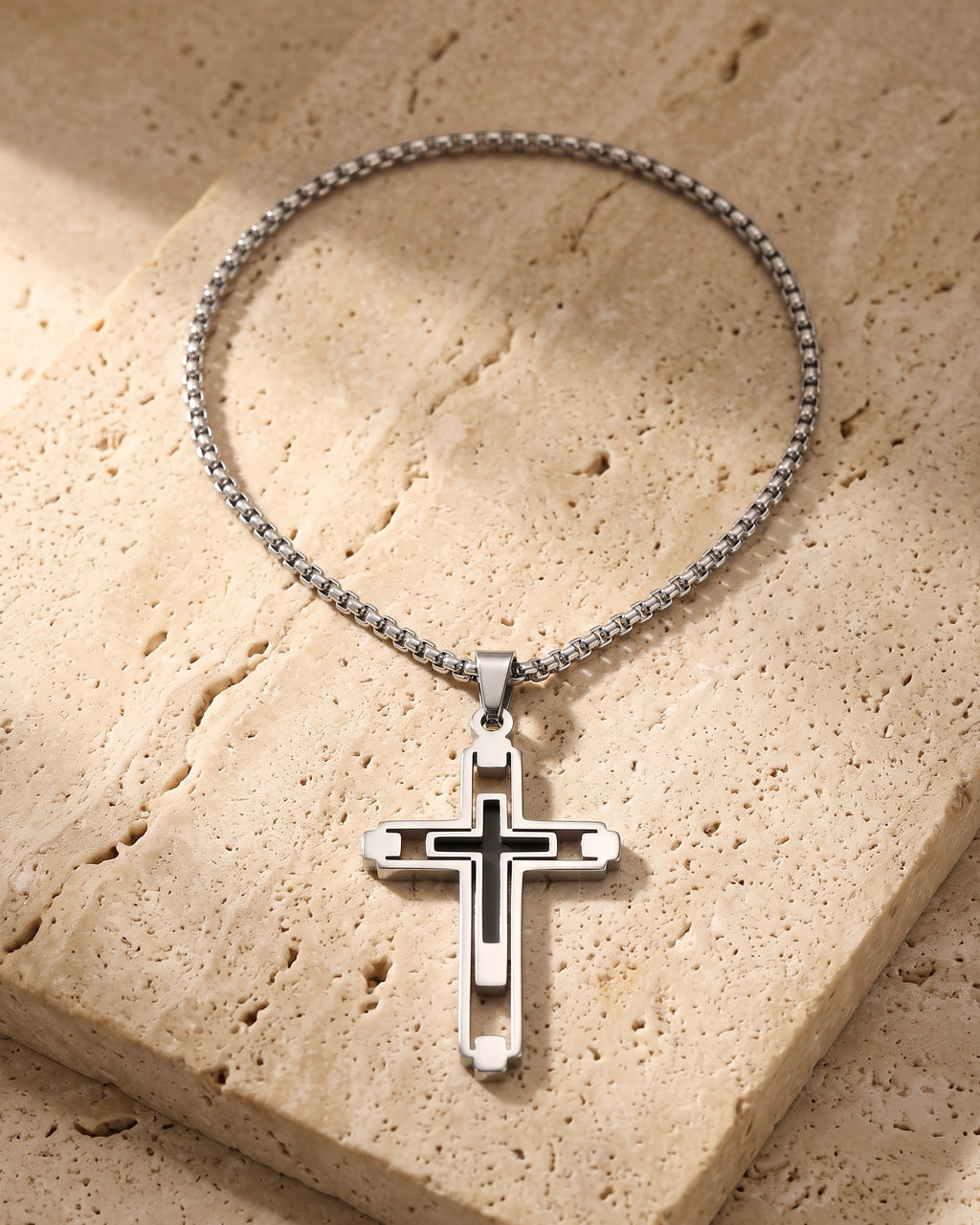 The whole silver-tone Atlas Hollow Geometric Cross Necklace lying on warm travertine stone