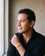 Man in an open-collar black shirt by a window wearing the gold-tone Atlas iced tennis bracelet