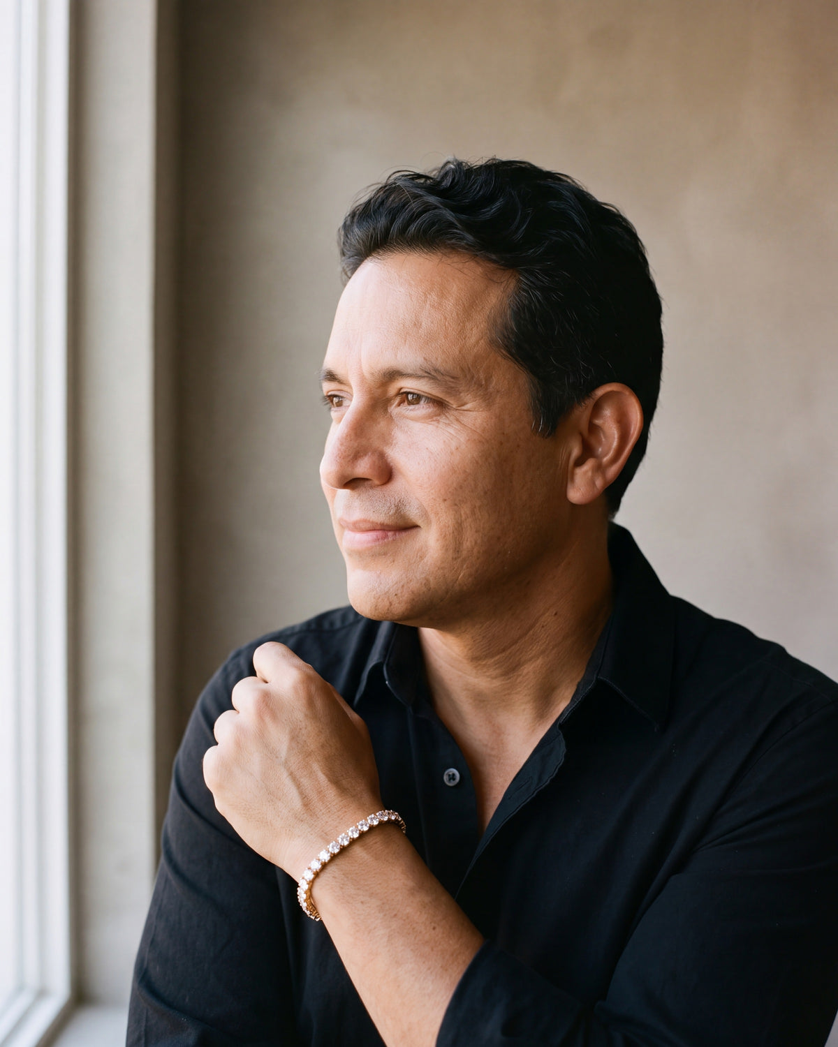 Man in an open-collar black shirt by a window wearing the gold-tone Atlas iced tennis bracelet