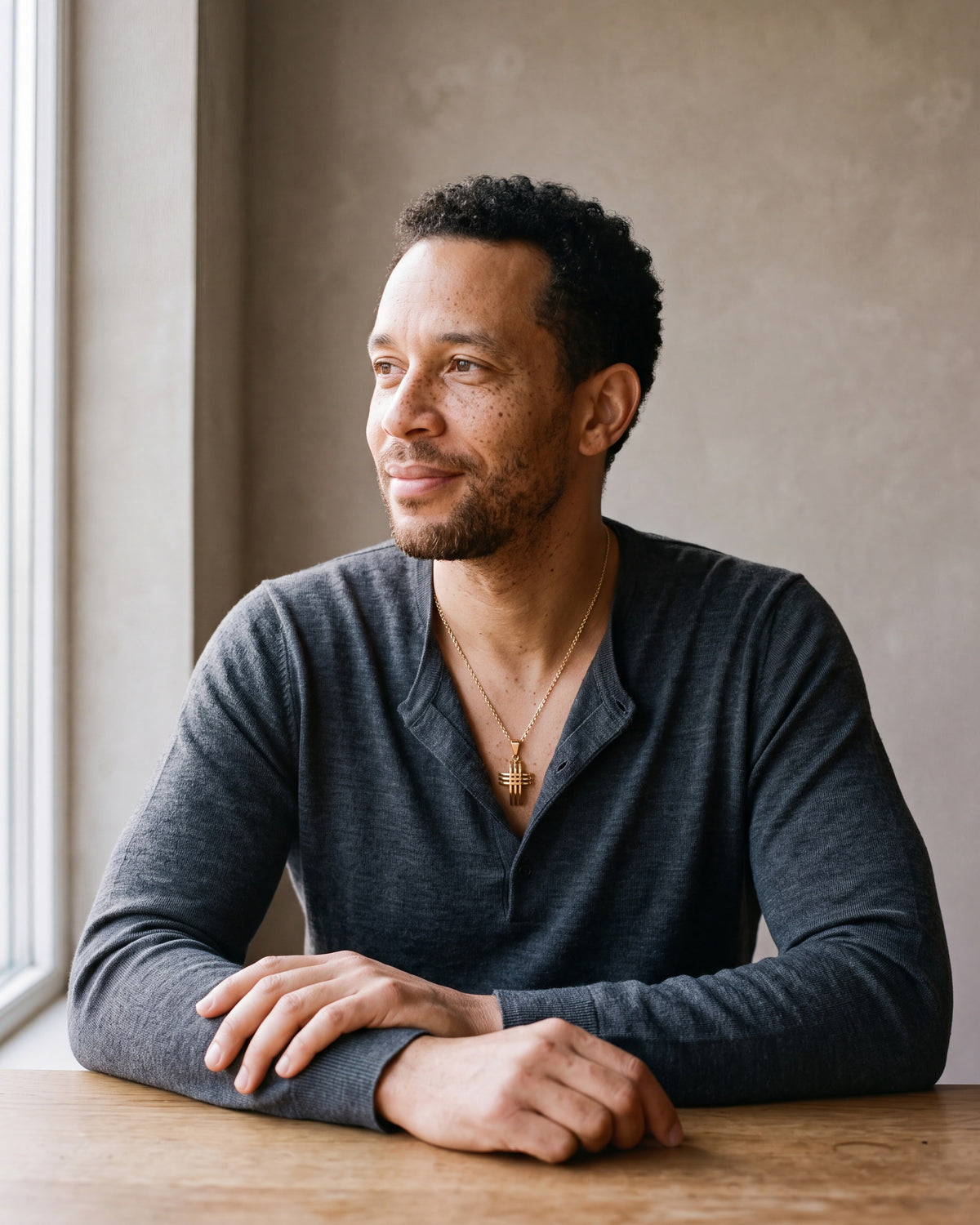 Man in a fine-gauge charcoal-grey merino knit with a henley neckline wearing the gold-tone Atlas Interlocking Cross Pendant Necklace