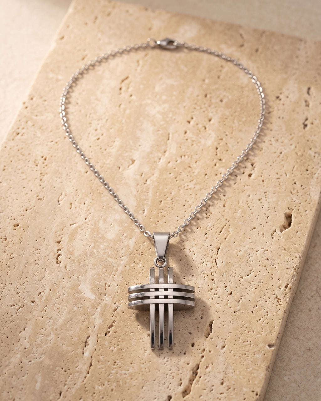 The whole silver-tone Atlas Interlocking Cross Pendant Necklace lying on warm travertine stone