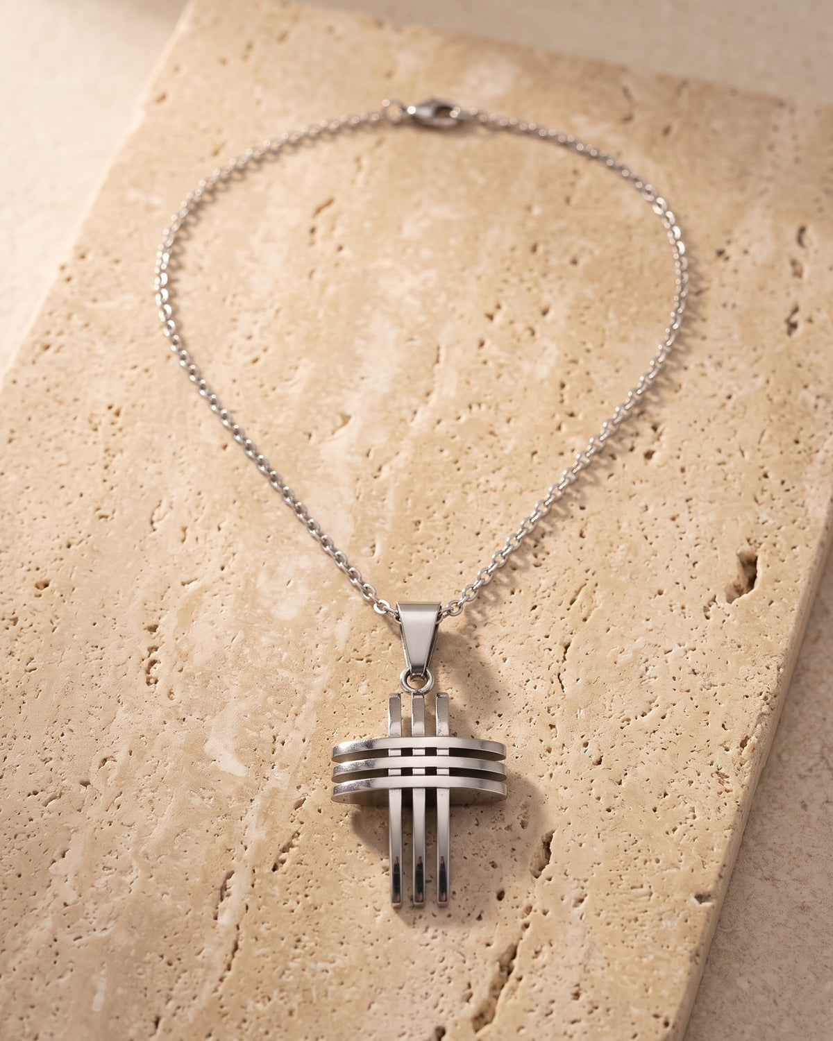 The whole silver-tone Atlas Interlocking Cross Pendant Necklace lying on warm travertine stone