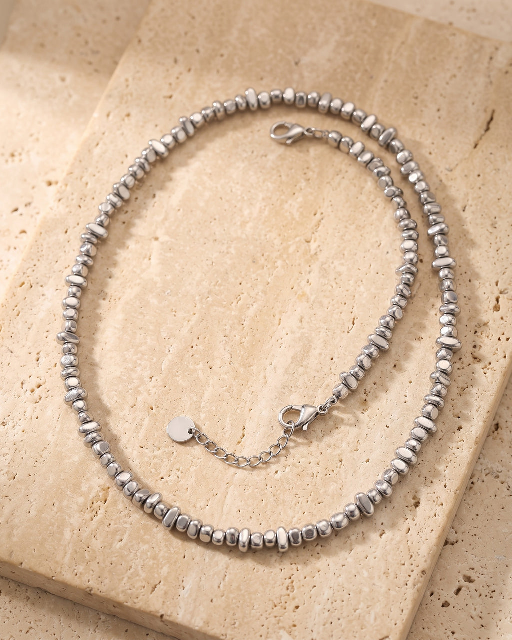 The whole silver Atlas irregular bead chain lying on warm travertine stone