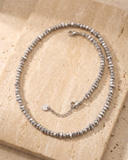 The whole silver Atlas irregular bead chain lying on warm travertine stone