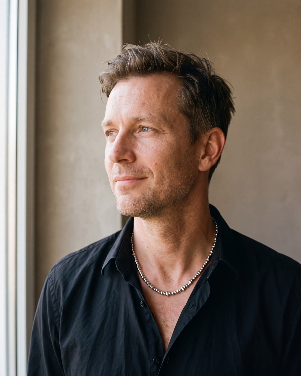 Man in a black fine cotton shirt by a window wearing the silver Atlas irregular bead chain